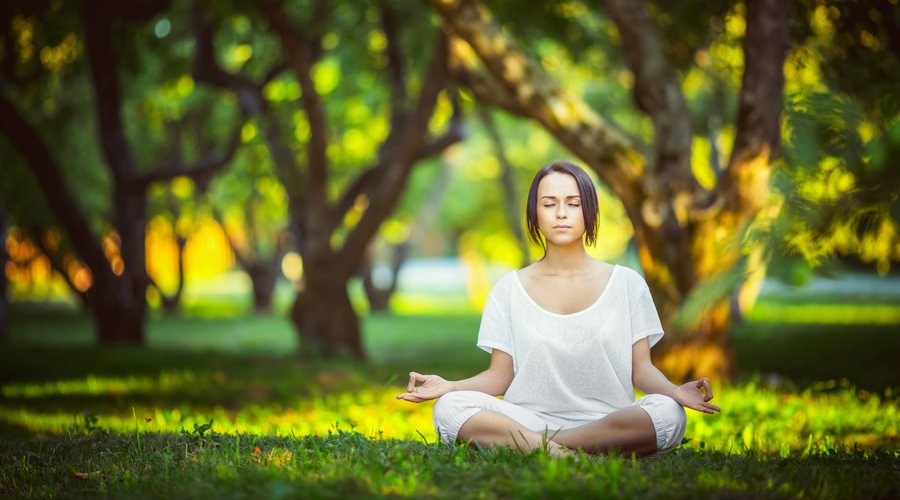 A woman meditating on the grass in a sunny green park