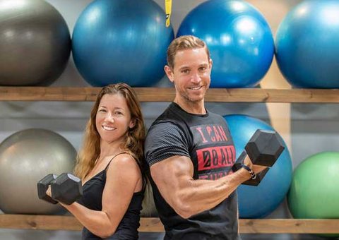 A smiling couple lifting dumbbells in a fitness studio